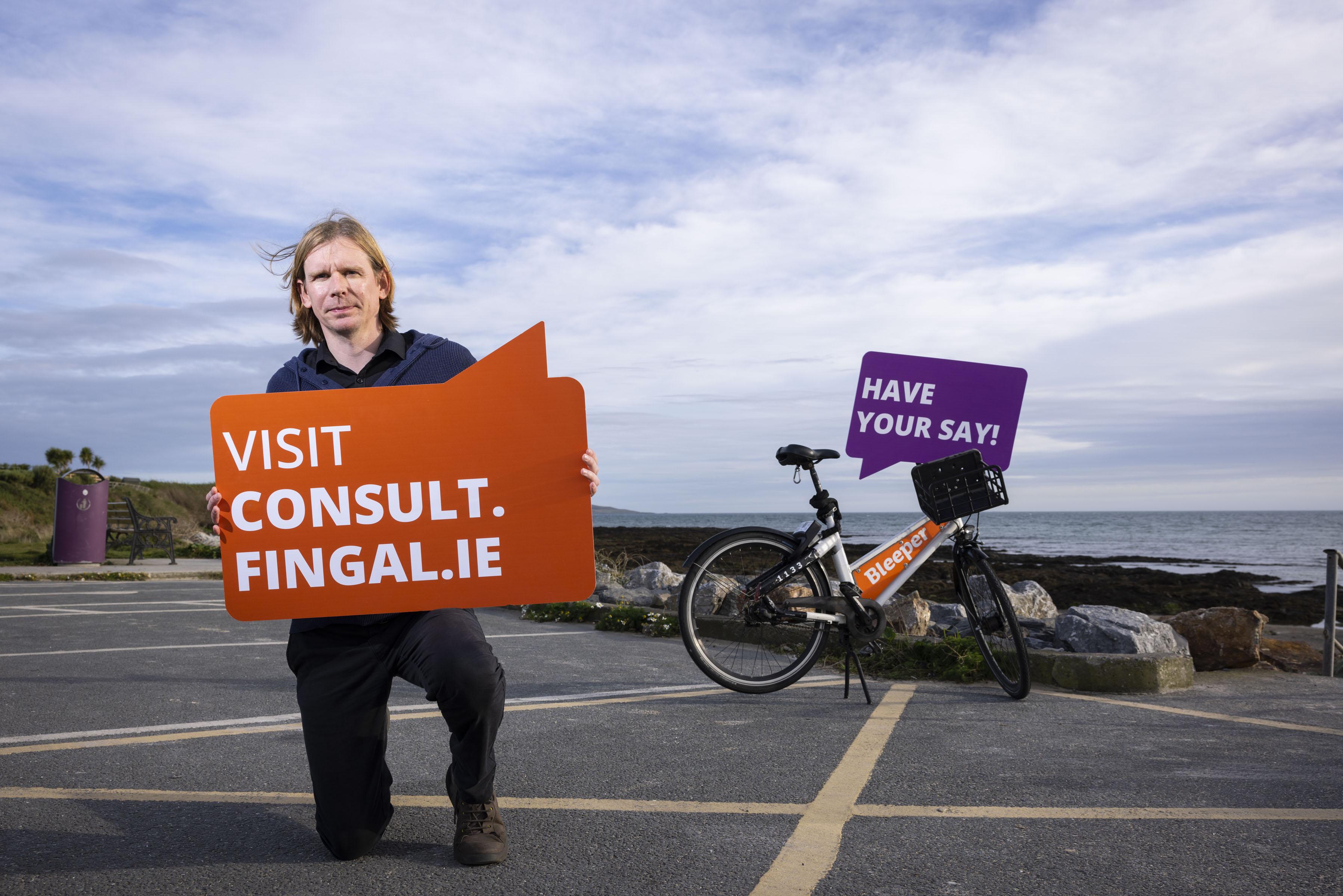 Man kneels with sign in hands saying consult.fingal.ie