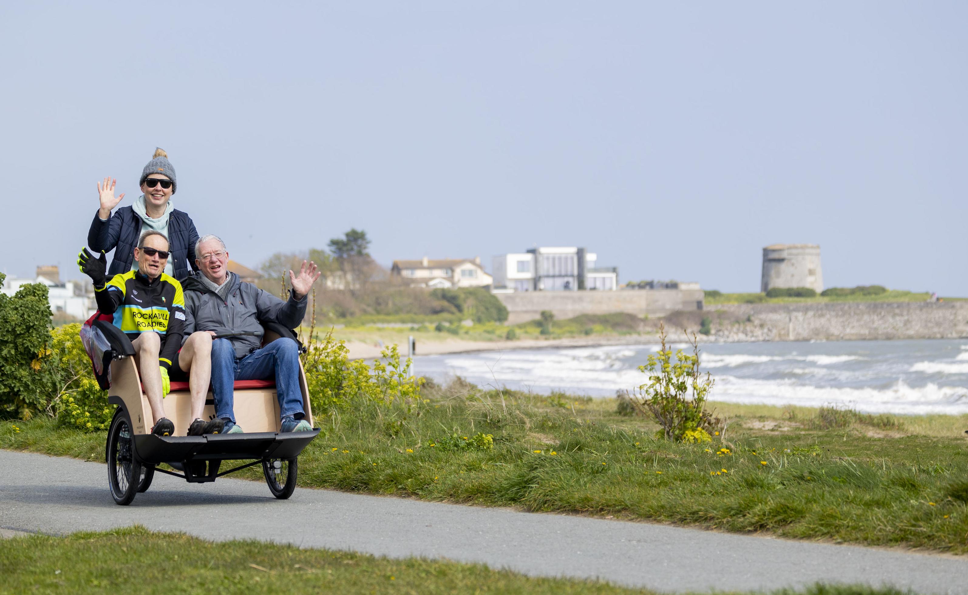 two men in trishaw seated with female cyclist to rear beach scene 