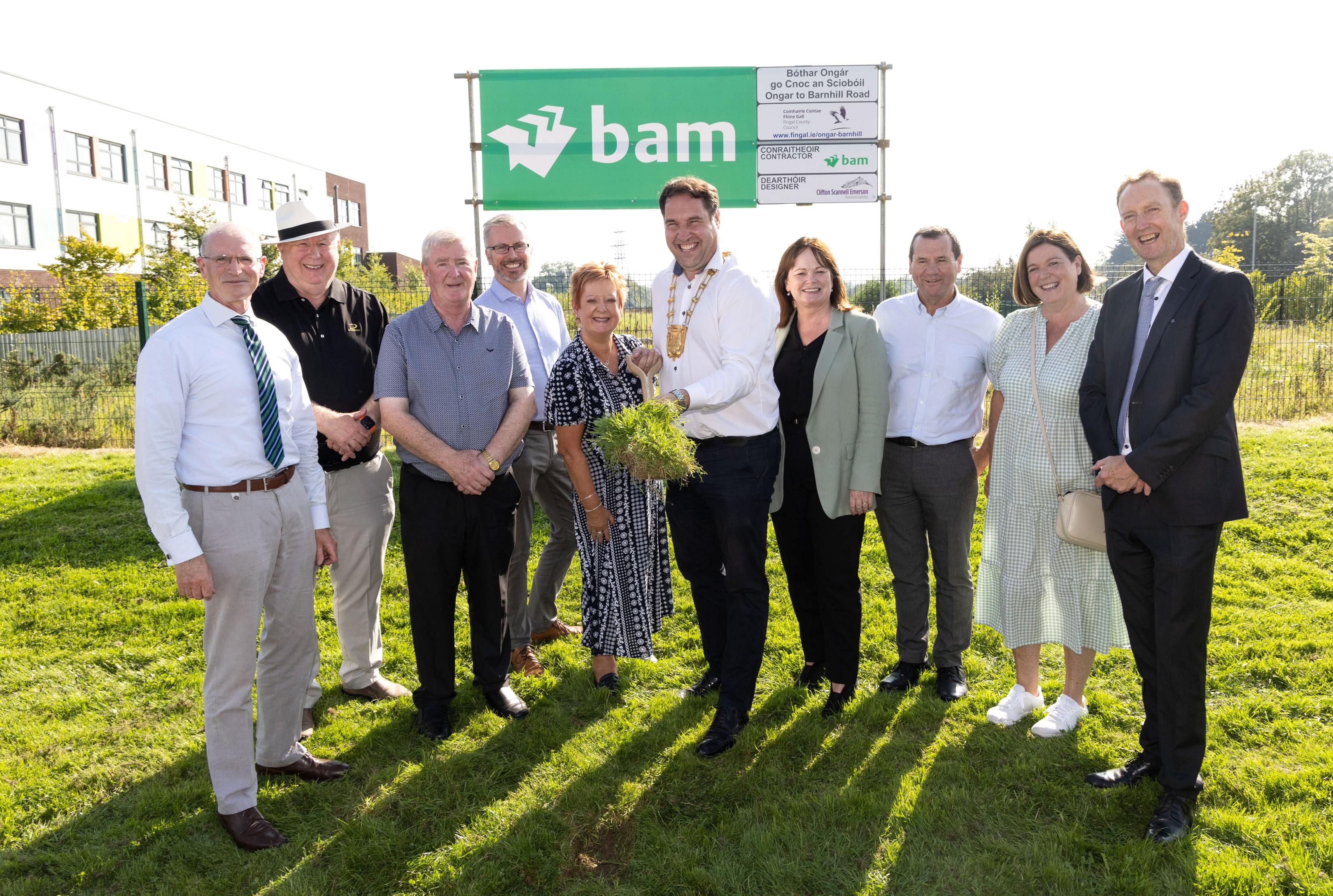 Mayor turns sod on spade surrounded by men and women standing on grass verge