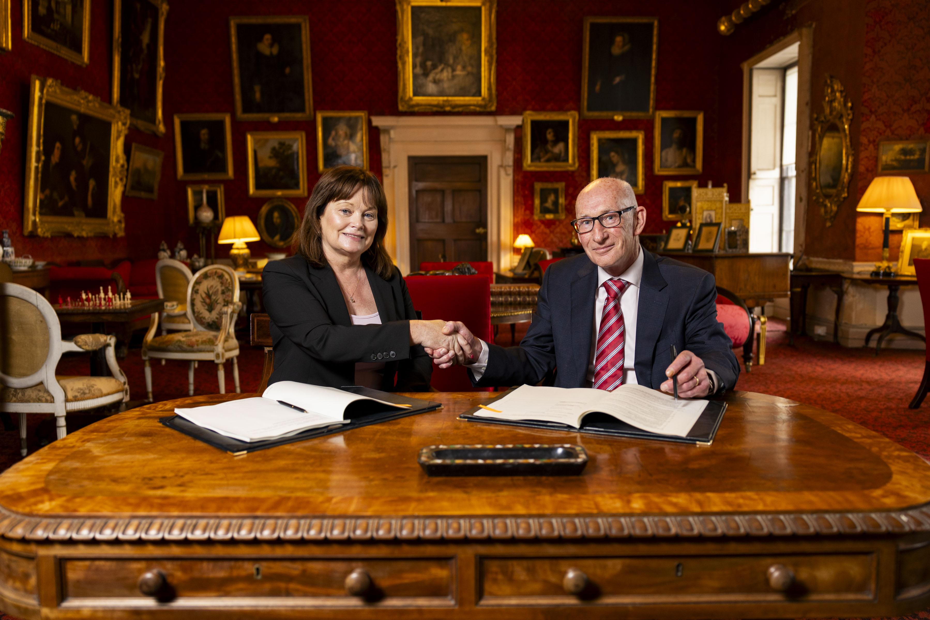 Man and woman shake hands over contract, seated at table