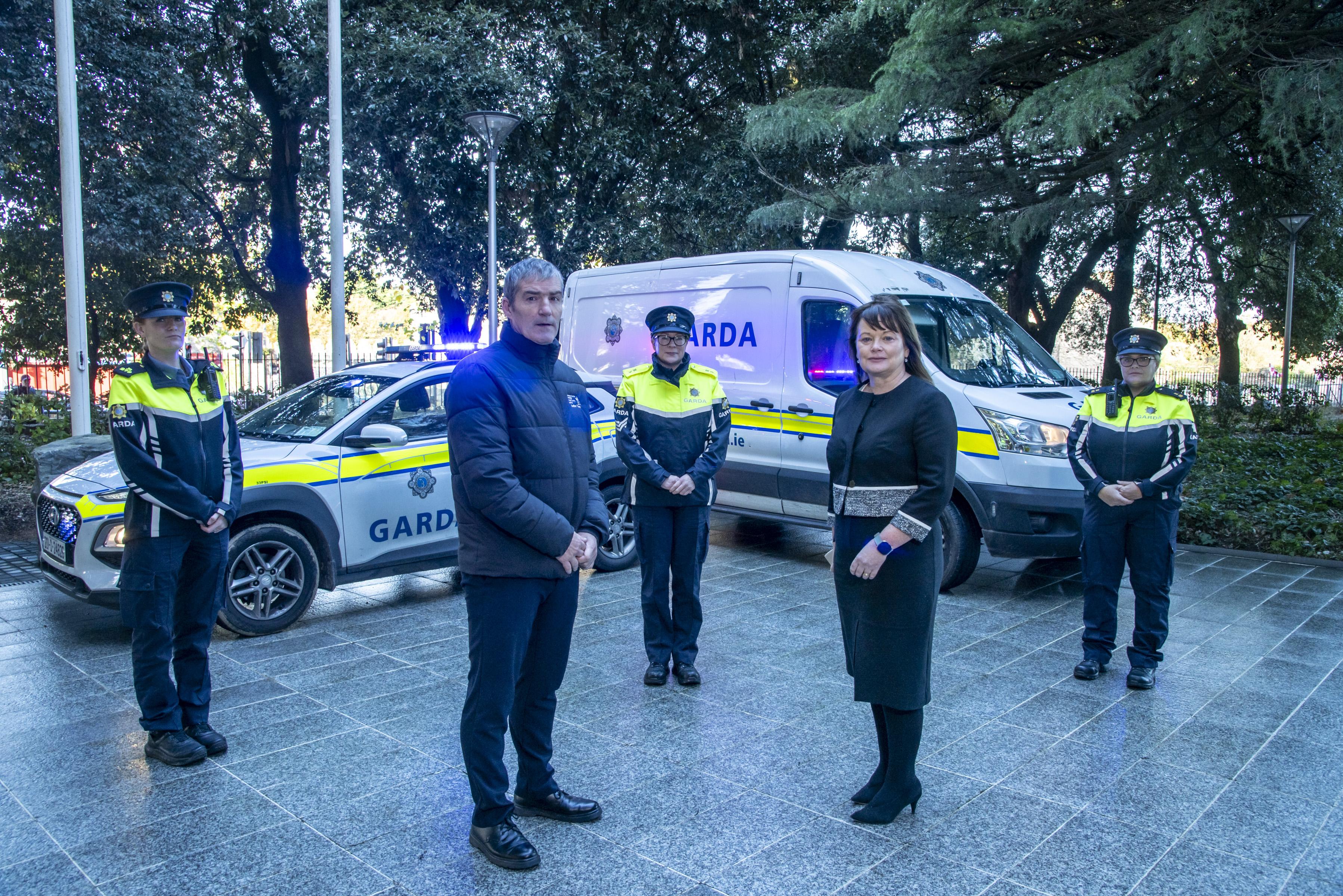 Sombre group of Gardai and staff standing in front of lit garda vehicles